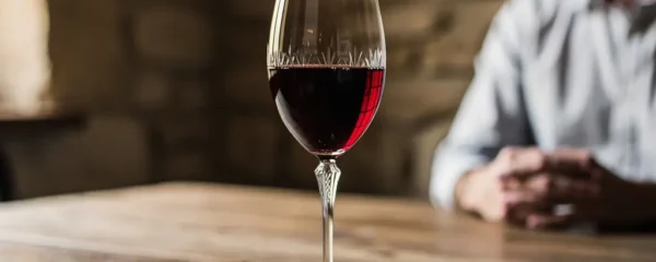 Verre en cristallin rempli de vin rouge sur table en bois, lumière traversant le liquide